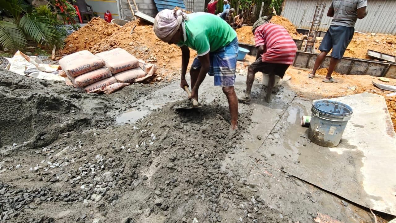 A worker mixes concrete on the ground by hand.