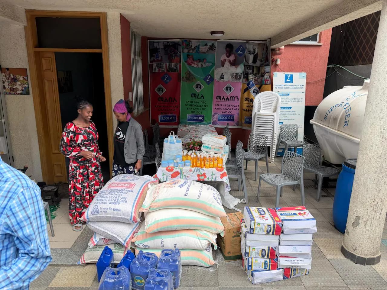 Sacks of flour and macaroni, water jugs and boxes of supplies set out under a porch.